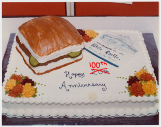 Sheet cake with hamburger replica made of cake, edited to say "Happy 100th Anniversary"